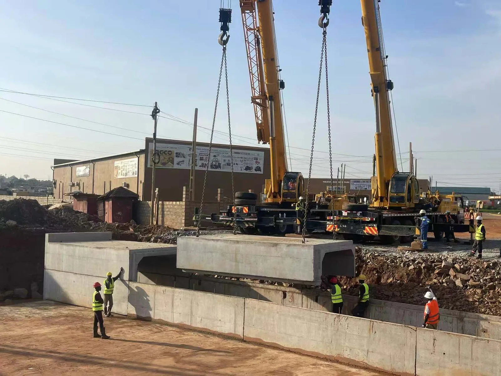 Two cranes lifting a precast box culvert into an excavated channel